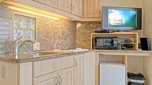 Una cocina compacta con encimera de granito, microondas integrado, un refrigerador pequeño y un televisor montado sobre la encimera.