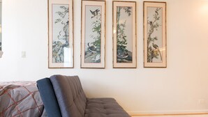 Una habitación con un sofá gris, una cama con ropa de cama estampada y tres cuadros en la pared.