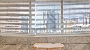Una habitación con ventana que da a un paisaje urbano, una pequeña mesa de madera y dos sillas.