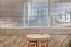 Ein Zimmer mit Fenster und Blick auf die Stadt, ein kleiner Holztisch und zwei Stühle.