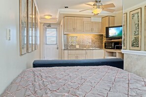 A compact bedroom with a bed, a ceiling fan, and a kitchenette with a TV. - Modern Studio w/Direct Sundeck Access, Kitchenette, and AC– Waikīkī Grand #1001 (Honolulu)