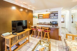 Ein Wohnzimmer mit Fernseher, Couchtisch und Küchenbereich mit Bar und Stühlen.