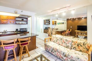 A modern kitchen with a bar area, a sofa with floral upholstery, and a large mirror reflecting the room. - Sundeck Studio w/ Kitchenette - Waikīkī Grand 1003 (Honolulu)