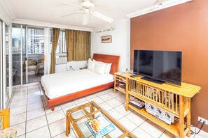 Ein Hotelzimmer mit einem Bett, einem Fernseher auf einem Holzboden, einem Glastisch und Blick auf die Stadt durch große Fenster.