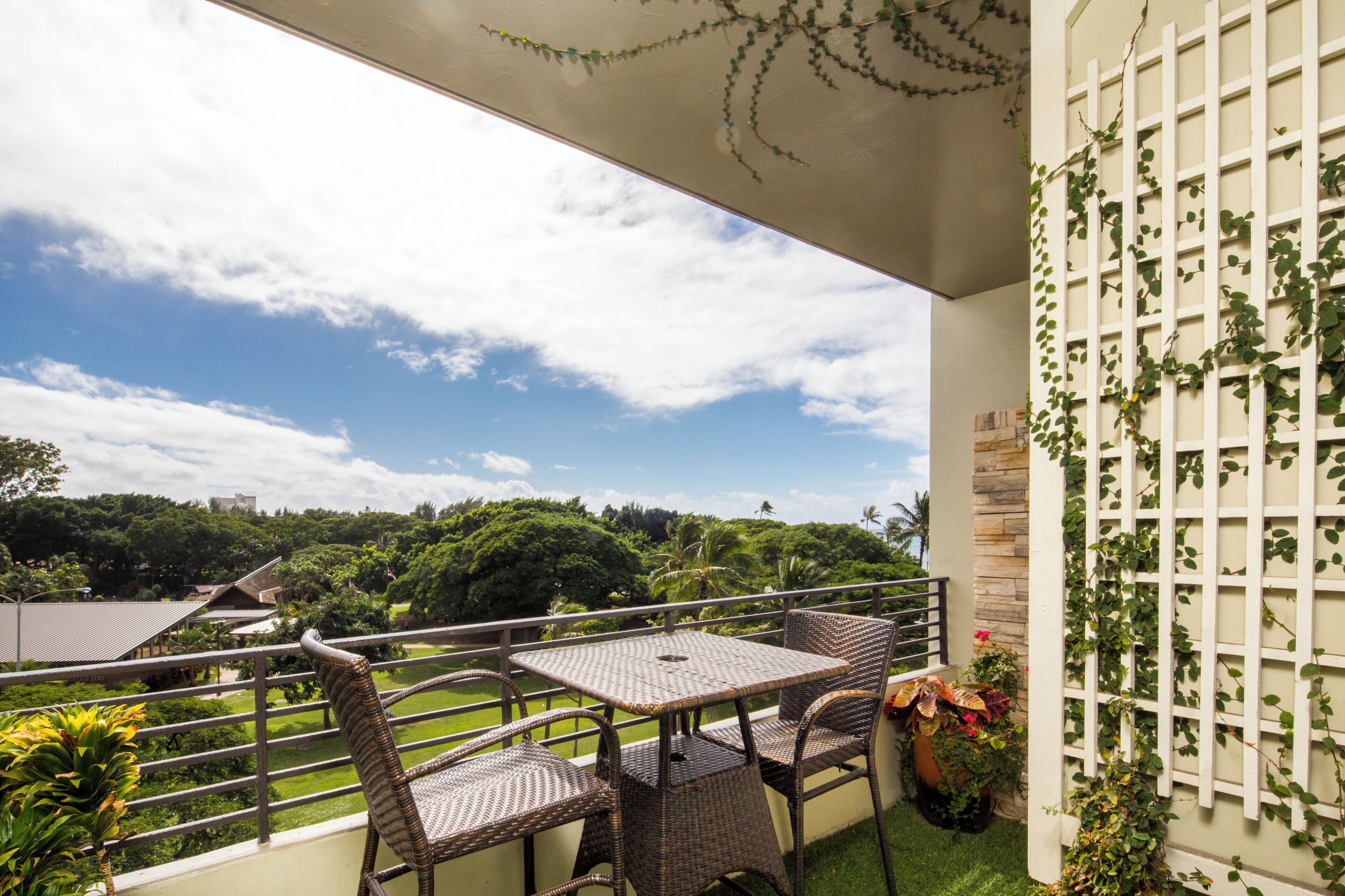 A balcony with wicker furniture, a view of greenery, and a white trellis with climbing plants.