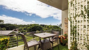 Uma varanda com mobiliário de vime, vista para o verde e um treliça branca com plantas trepadoras.