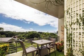 Ein Balkon mit Korbmöbeln, Blick ins Grüne und ein weißes Spalier mit Kletterpflanzen.