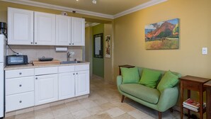Eine Küche mit weißen Schränken, einer Kaffeemaschine und einem Toaster. Ein grünes Sofa und ein Bild hängen an der Wand.