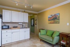 Eine Küche mit weißen Schränken, einer Kaffeemaschine und einem Toaster. Ein grünes Sofa und ein Bild hängen an der Wand.