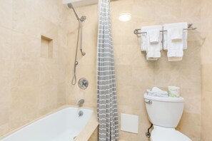 Een badkamer met bad, douche, toilet en handdoekhouder.