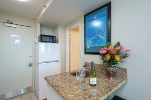 A kitchen with a granite countertop, a wine bottle, and a vase of flowers. - Ocean View Studio with Kitchenette - Waikīkī Grand #910 (Honolulu)