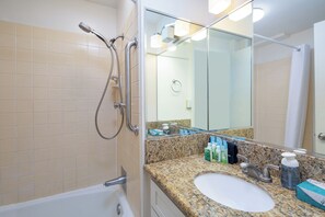 A bathroom with a white sink, granite countertop, and a glass shower enclosure. - Ocean View Studio with Kitchenette - Waikīkī Grand #910 (Honolulu)