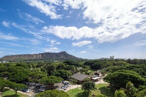A lush park with a mountain in the background, a parking area, and a building with a flat roof. - Ocean View Studio with Kitchenette - Waikīkī Grand #910 (Honolulu)