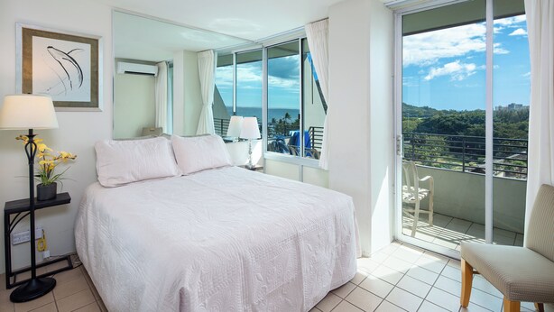 Ein Hotelzimmer mit einem großen Bett, einem Balkon mit Blick auf die Stadt und einer Zimmerpflanze.