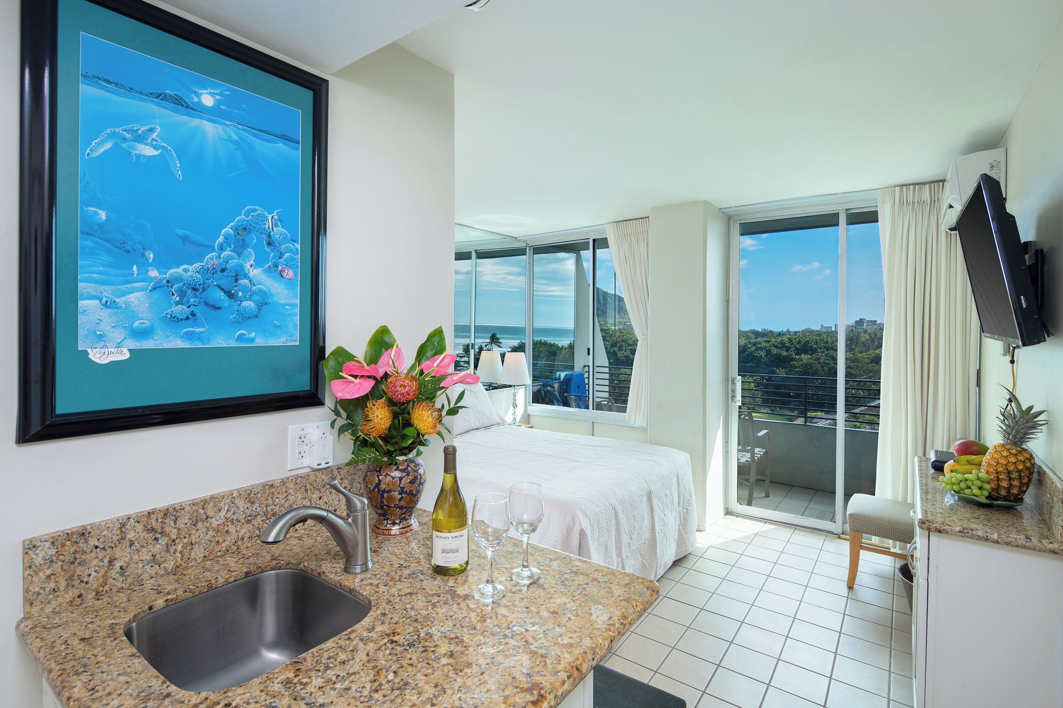 Une chambre d’hôtel avec un coin cuisine, un lit, un balcon avec vue et un téléviseur fixé au mur.