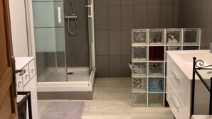 Casa de banho moderna com cabine de duche em vidro, uma pia branca e um móvel de armazenamento com gavetas.