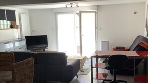 Uma sala de estar com sofá, televisão, mesa de jantar e cozinha.