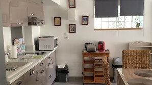 Uma cozinha moderna com eletrodomésticos de aço inoxidável, área de jantar com mesa de madeira e cadeiras de vime, e uma pequena janela com vista para o verde.