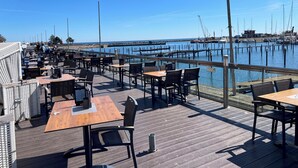 Eine Holzterrasse mit Tischen und Stühlen mit Blick auf einen Hafen voller Boote.