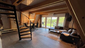 Ein geräumiges Loft mit einer Treppe, einer Couch, einem Esstisch und einer großen Schiebeglasdoor zu einem Garten.