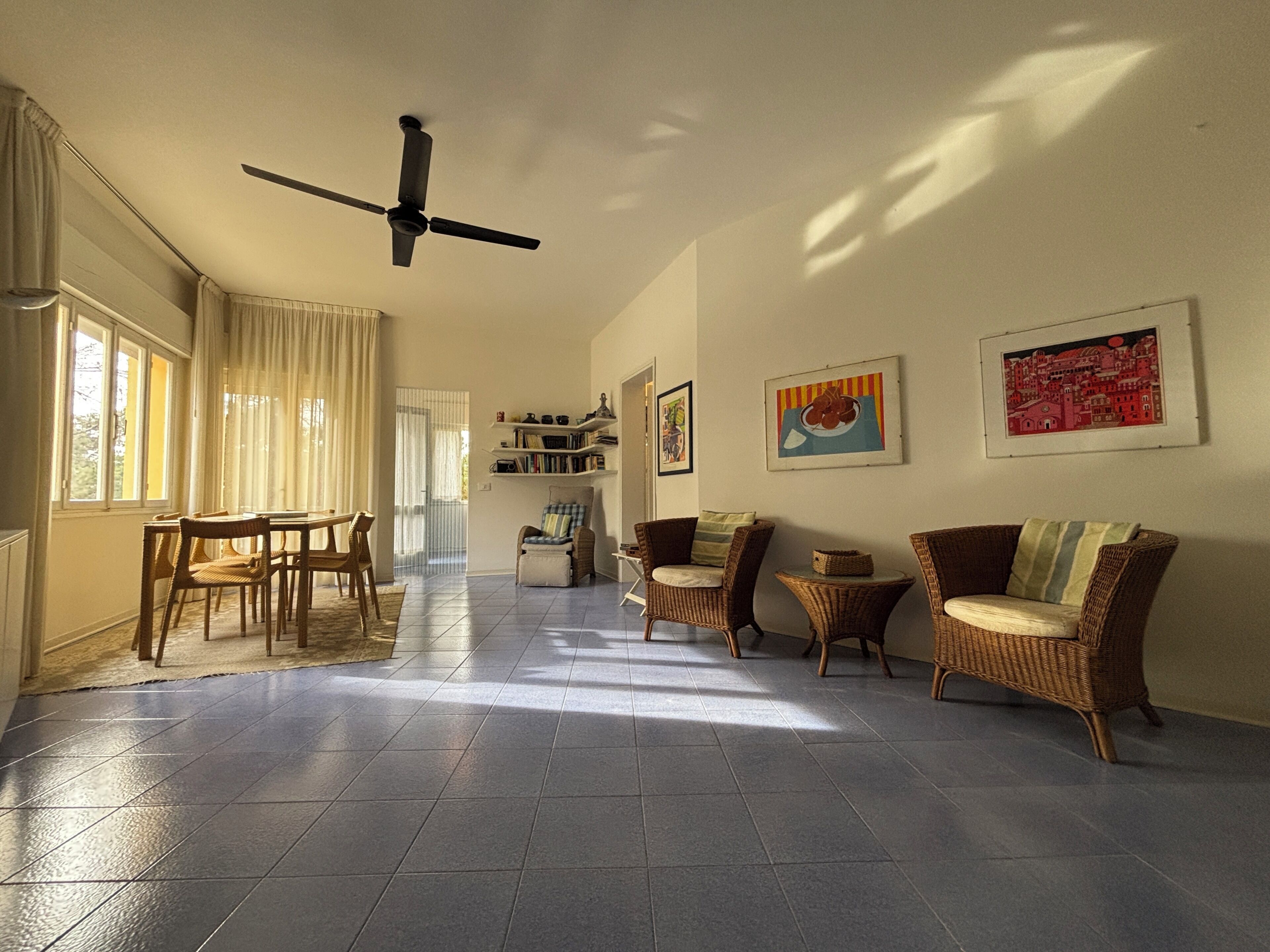A spacious living area with a ceiling fan, a dining table with chairs, wicker furniture, and artwork on the walls.