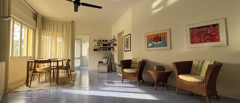 A spacious living area with a ceiling fan, a dining table with chairs, wicker furniture, and artwork on the walls.