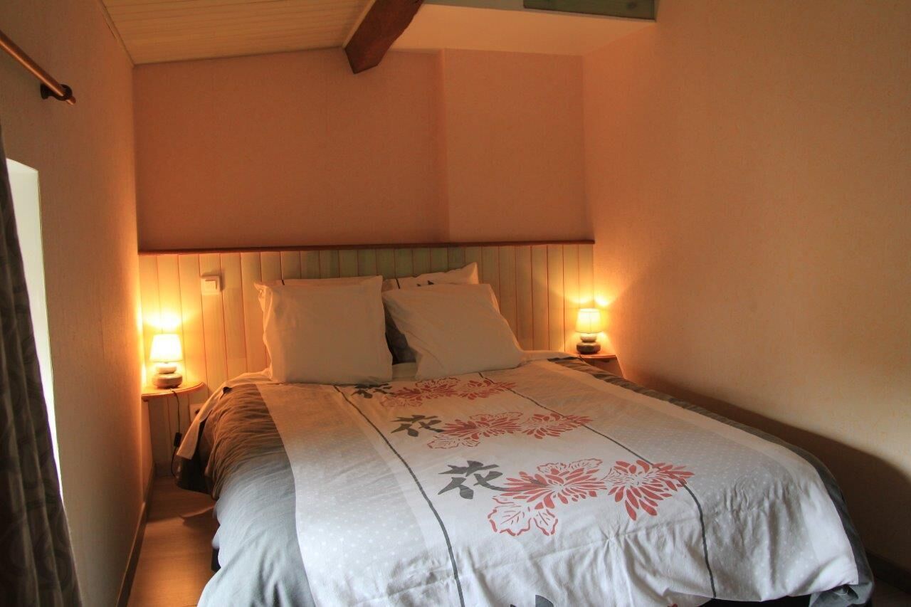 A narrow hotel room with a bed, two bedside lamps, and a window with curtains.