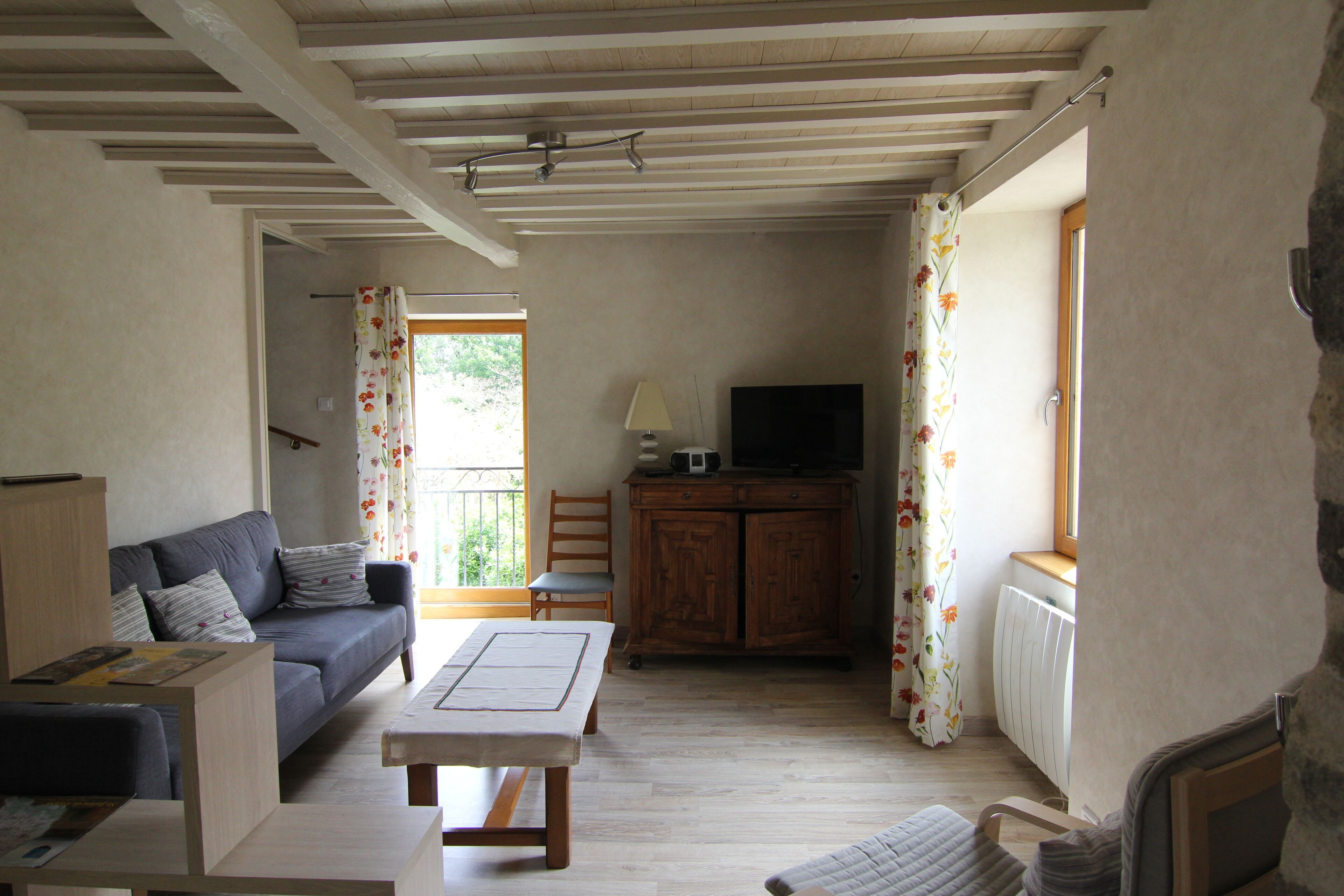 Ein Zimmer mit einer Couch, einem Tisch, einem Schrank, einem Fernseher und einem fenster mit Vorhängen.