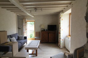 A room with a sofa, a table, a cabinet, a television, and a window with curtains. - 3-star, fully equipped vacation rental in a quiet, rural setting (Saint-Julien-de-Coppel)