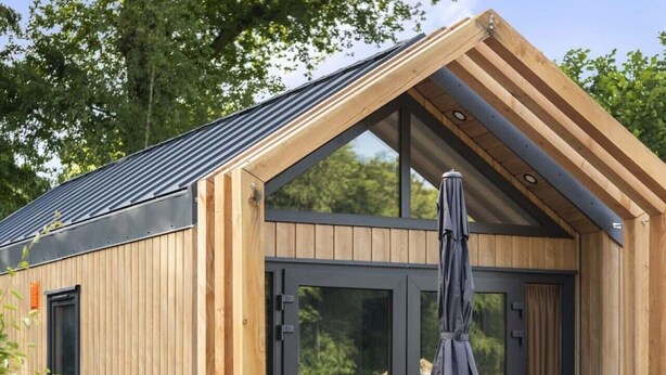 Une cabane en bois avec une grande porte vitrée, une terrasse avec une table et des chaises, et un jardin.