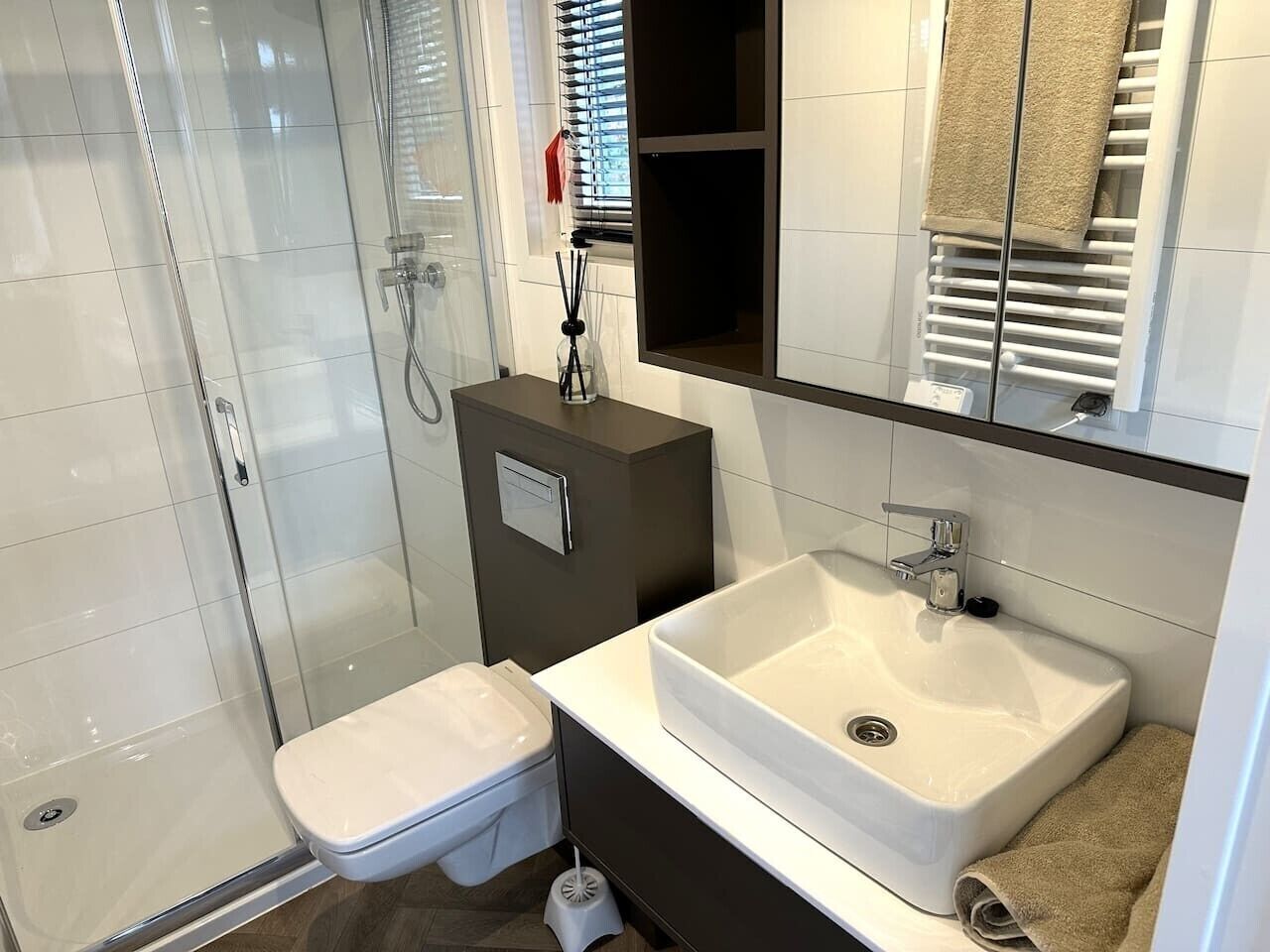 Ein modernes Badezimmer mit Duschkabine aus Glas, einer weißen Toilette, einem großen Waschbecken und einem Spiegel darüber.