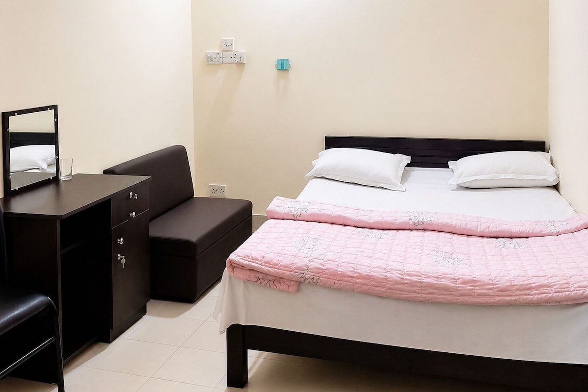 Una habitación de hotel con una cama, un escritorio, una silla, un espejo y una mesita de noche.