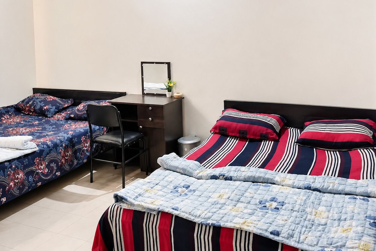 Un dormitorio con dos camas individuales, un escritorio con silla, un ventilador de techo y una ventana pequeña.