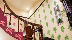 Una escalera con barandilla de madera, una pared curva decorada con motivos florales verdes y un pequeño estante con una planta.