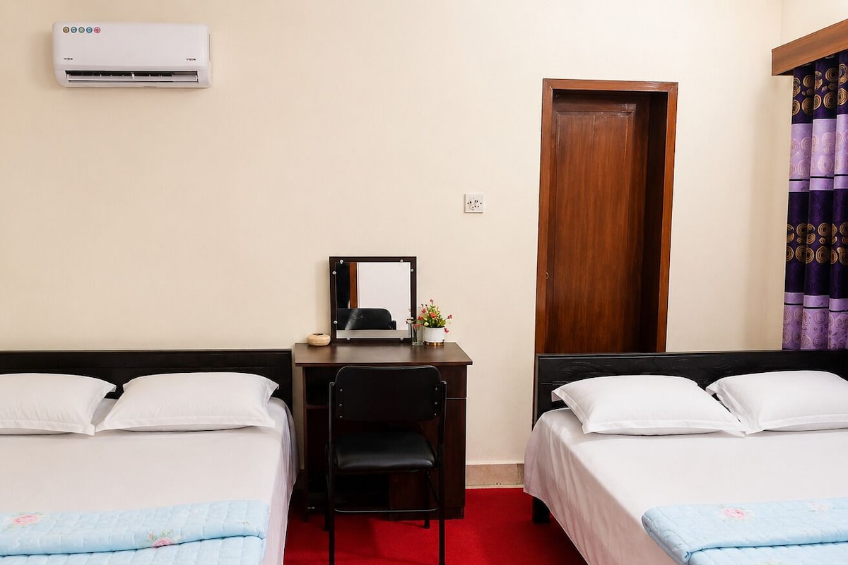 Habitación de hotel con dos camas, un escritorio, una silla, un espejo y un equipo de aire acondicionado.