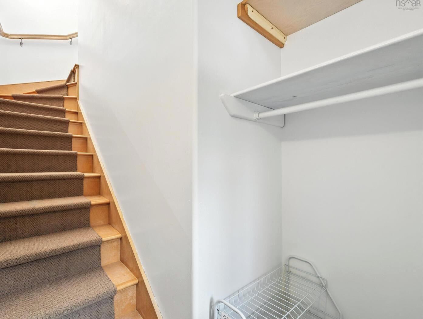 A staircase with carpeted steps and a metal handrail, leading to a white wall with a wooden shelf and a metal wire shelf.