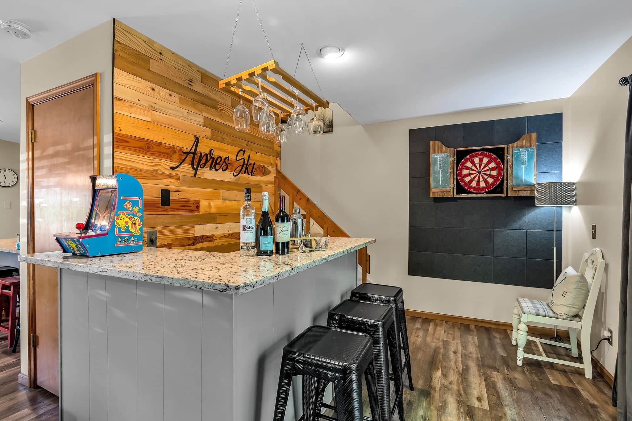 A kitchen with a wooden accent wall, a dartboard, and a bar area with stools.