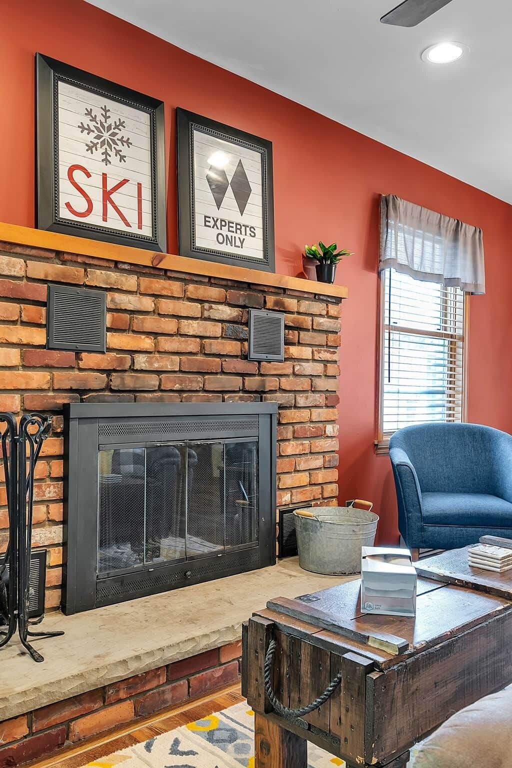 A living room with a brick fireplace, framed signs above it, a blue armchair, and a coffee table.