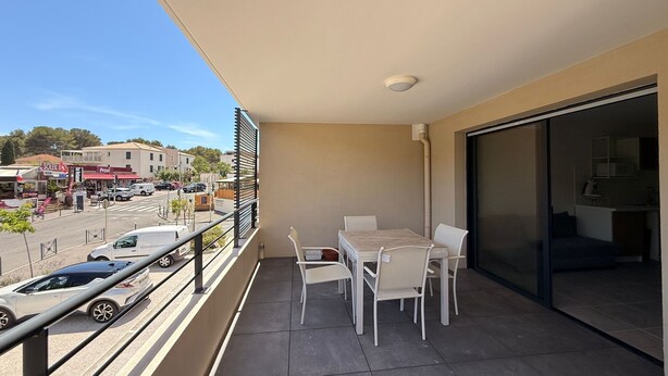 Un balcon avec une table et des chaises, une vue sur la rue et un immeuble avec une enseigne.