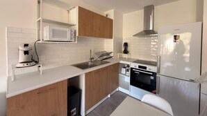 Une cuisine moderne avec des plans de travail blancs, des armoires en bois, un four à micro-ondes, une cuisinière et un réfrigérateur.