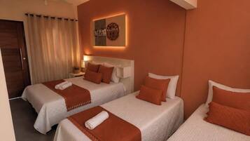 A hotel room with three beds, a ceiling fan, a wall clock, and a small table with a plant.