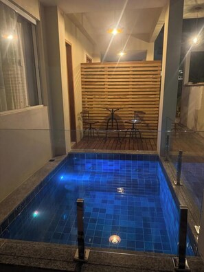 Una piscina con azulejos azules, una valla de madera y una zona de estar con sillas y una mesa.