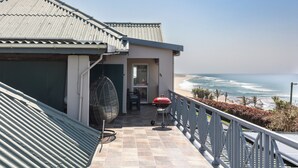 Een balkon met uitzicht op de oceaan, een barbecue en een hangstoel.