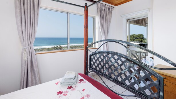 Een slaapkamer met een bed, uitzicht op zee en een balkon.