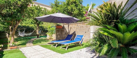 Une terrasse avec deux chaises longues, un fauteuil suspendu et une petite table.