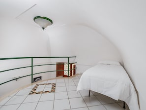 A small, white-walled room with a curved ceiling, a bed with white bedding, a green railing, and a small wooden cabinet. - De Vivo Realty - Golden Garden Sorrento. (Meta)