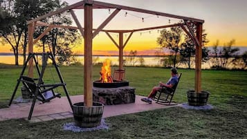 A wooden gazebo with a fire pit and seating area, overlooking a body of water.
