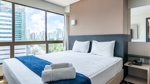 A modern hotel room with a large bed, a city view, a desk with a phone, and a mirror. - Home Stay #606 - Studio in Recife by Carpediem (Recife)