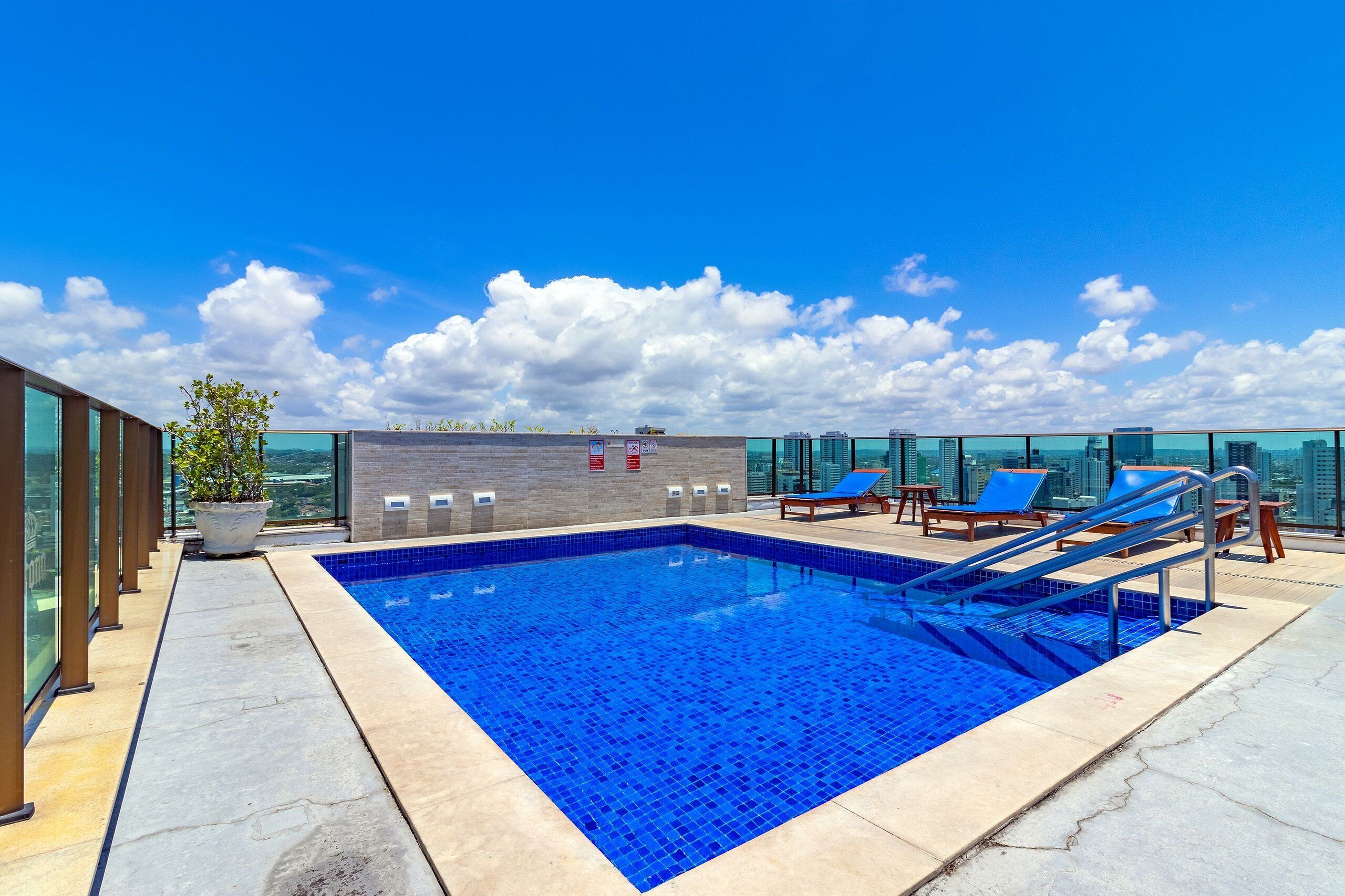 A rooftop pool with clear blue water, surrounded by lounge chairs and a potted plant.