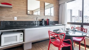 A modern kitchen with a black countertop, white cabinets, a red chair, and a dining table with a glass top. - Home Stay #606 - Studio in Recife by Carpediem (Recife)
